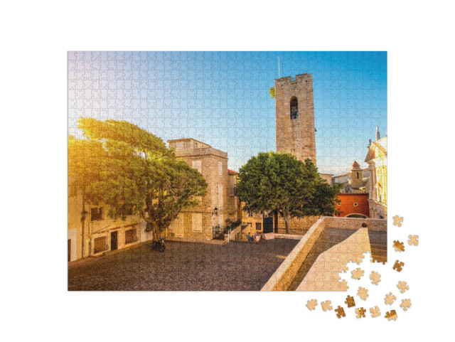 Puzzle de 1000 pièces « Place centrale avec tour et église dans le village côtier d'Antibes sur la Côte d'Azur en France »